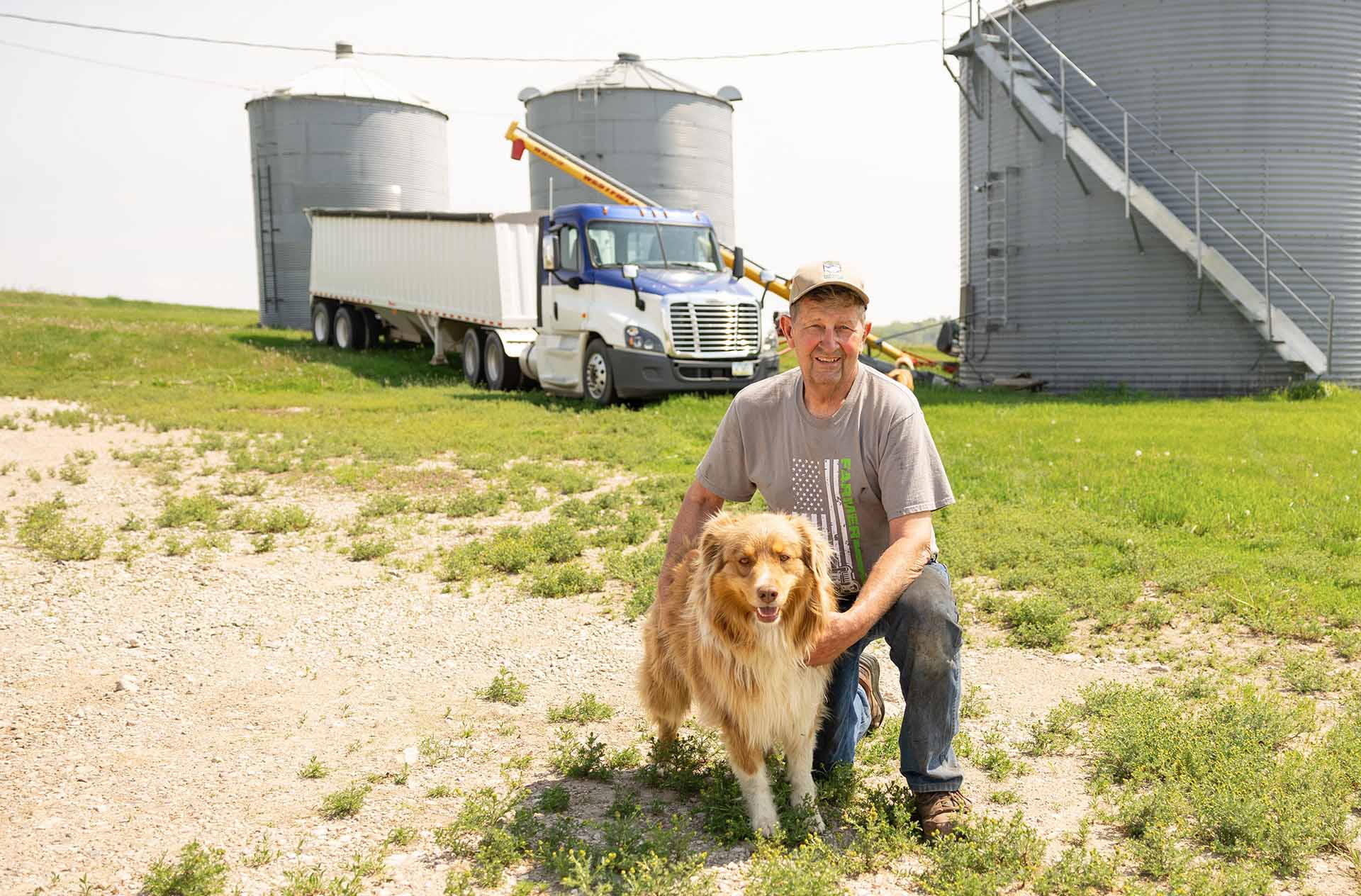 Farmer kneeling next to dog on farm